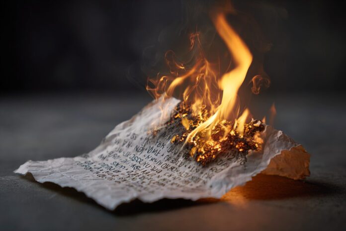 A burning sheet of paper with a 12-word seed phrase, symbolizing loss and risk.