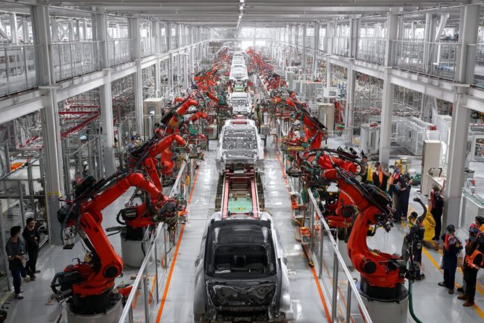 Tourists observe robotic arms assembling electric vehicles on a modern production line in China.