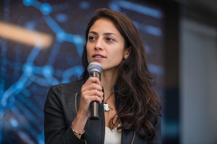 Mira Murati announcing the $2B seed round for Thinking Machines Lab, standing before a blurred background of investors.