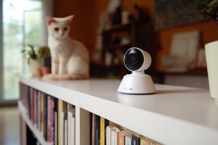 A close-up of the PetLibro Scout Smart Camera on a bookshelf overlooking a curious cat.