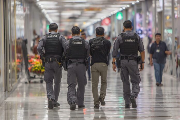 Thai police escorting a suspect at Don Mueang Airport after a bitcoin fraud arrest.