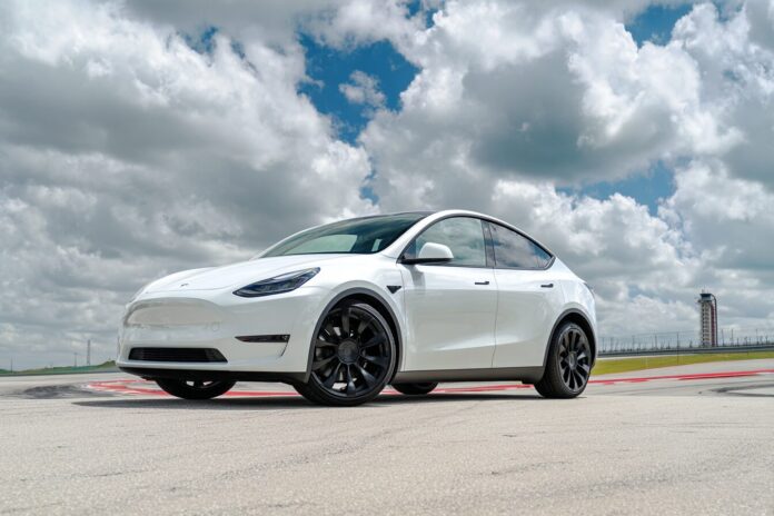 A Tesla Model Y exiting the Gigafactory Texas lot, poised on an open road for its autonomous journey.