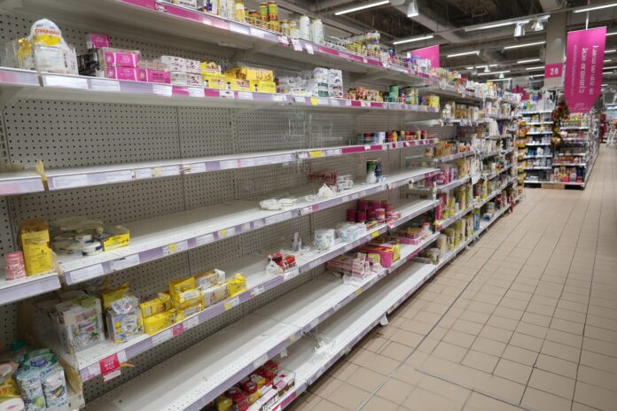 Rows of mostly empty grocery store shelves with a few remaining products.