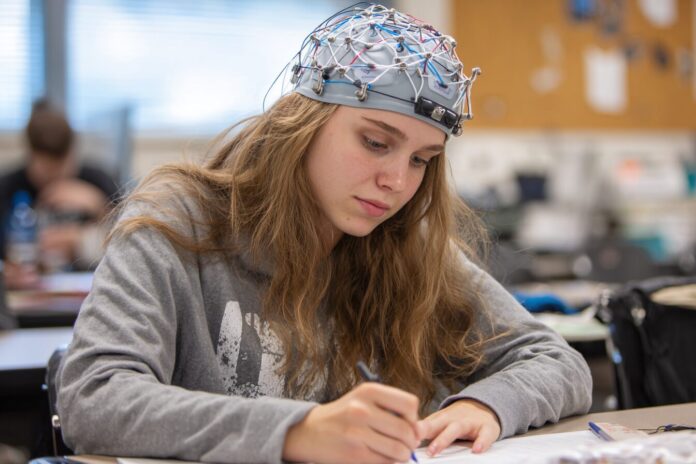 EEG headset on student writing in a classroom setting.