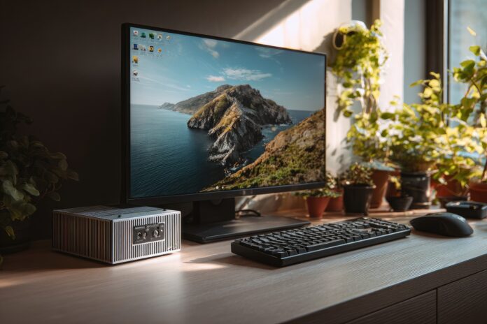 A compact Mini PC next to a monitor and keyboard on a tidy desk.