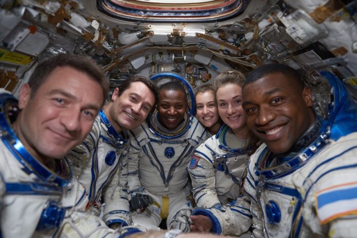 ISS crew and newly arrived astronauts floating in the Harmony module, all smiling and clustered in zero gravity.