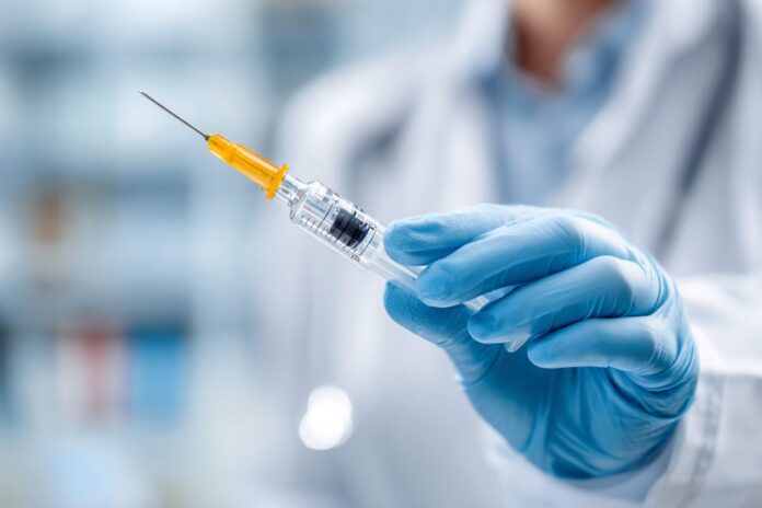 A close-up of a doctor's hand preparing a testosterone injection syringe in a clinical setting.