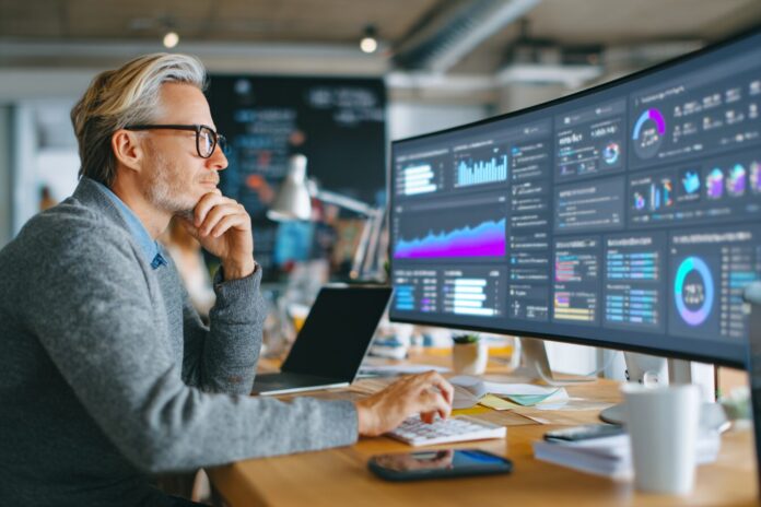 A busy professional at a desk, calmly overseeing an AI-powered dashboard as digital agents process emails and data in the background.