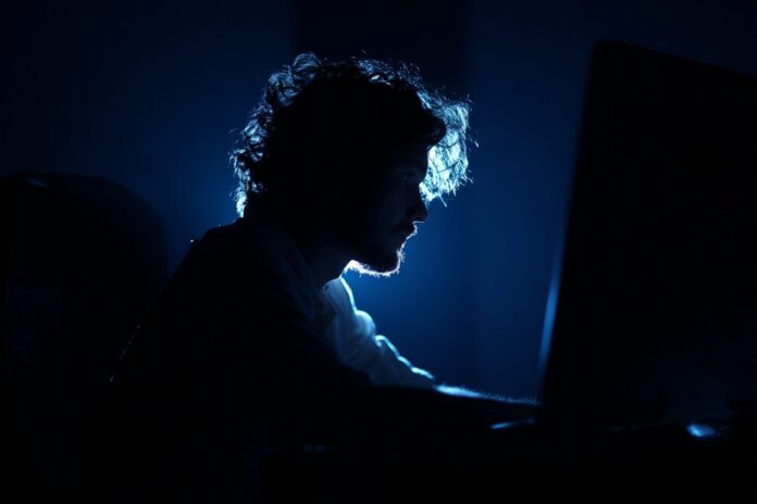 Isolated individual illuminated by the glow of a computer screen, surrounded by darkness