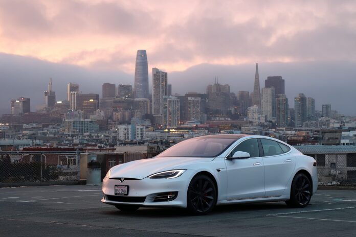 A Tesla car parked in San Francisco with city skyline in the background.