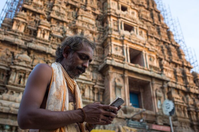 A devotee using the Sri Mandir app in front of an ancient temple, symbolizing the merger of tradition and technology.