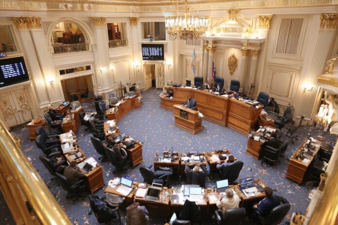 State legislators discussing new climate superfund bills in a modern assembly chamber