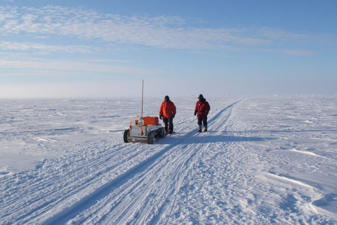 Scientists using ice-penetrating radar equipment on Greenland’s ice sheet under clear sky.