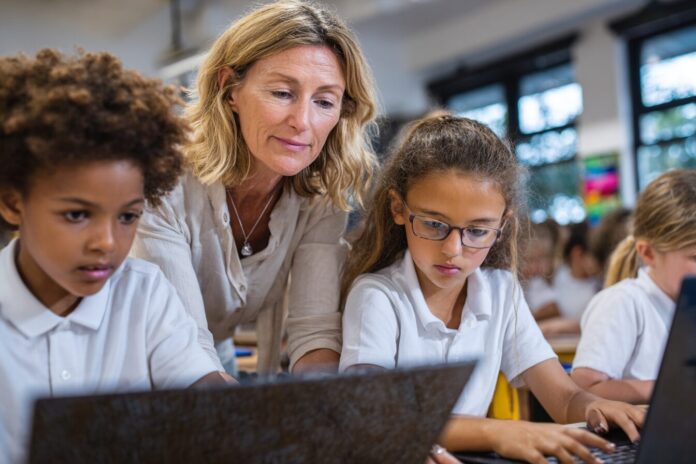 A teacher guiding students as they use laptops in a classroom, symbolizing the balance of AI tools and traditional learning.