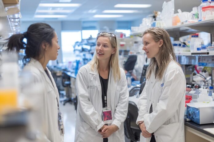 Three scientists discussing mitochondrial replacement therapy in a modern laboratory.