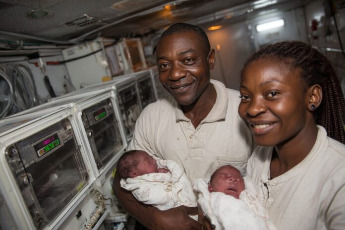 Two South African newborns held by their parents, mobile IVF lab equipment in the background