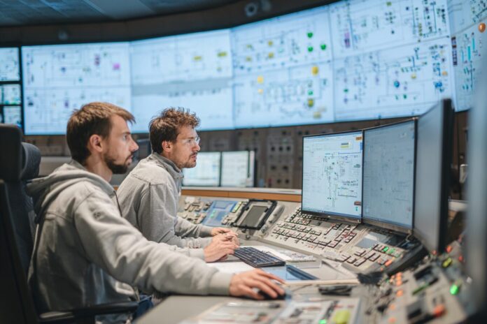 Two engineers reviewing AI-generated nuclear permit documentation in a control room