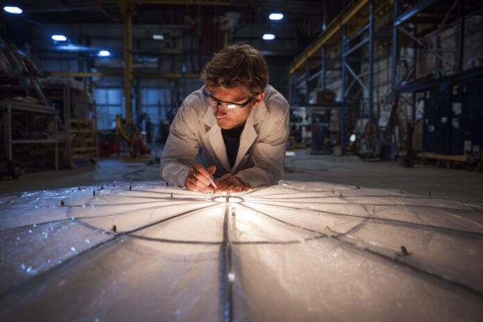 NASA researcher inspects sensor-equipped supersonic parachute during ground test, focusing on innovative fabric and embedded sensors.