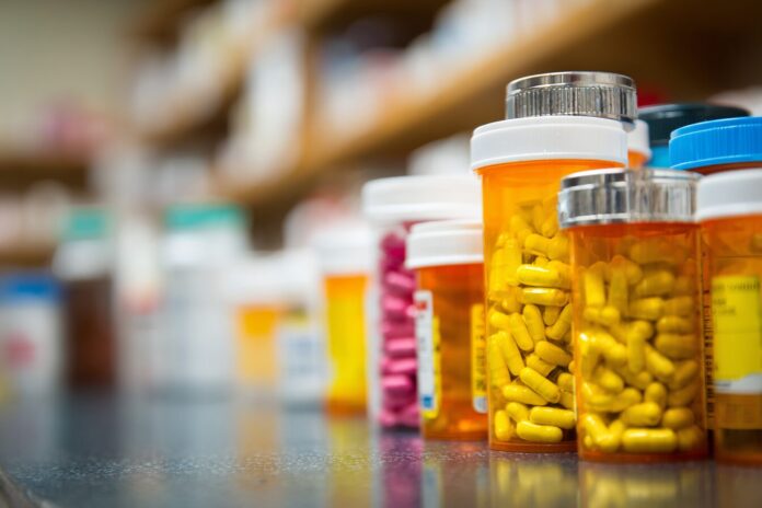Pile of prescription medication bottles grouped together on a pharmacy counter, representing high drug costs.