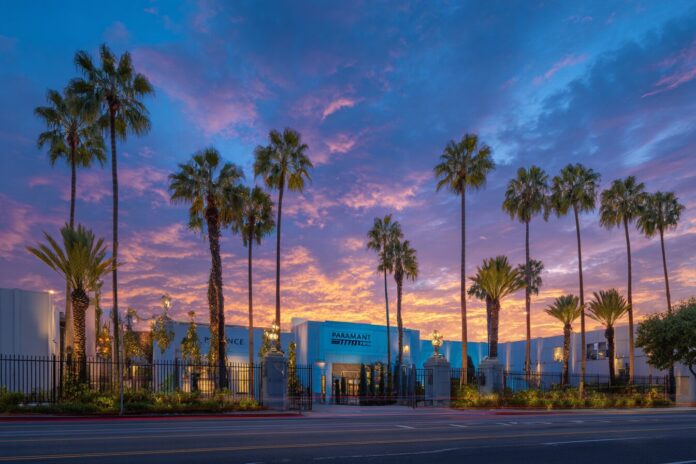 Exterior of Paramount Pictures' iconic Melrose Avenue studio lot at sunset, with Skydance and Paramount logos digitally blended over the gates.