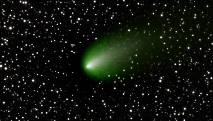 A telescopic image of interstellar comet 3I/ATLAS showing its fuzzy greenish coma against a star field.