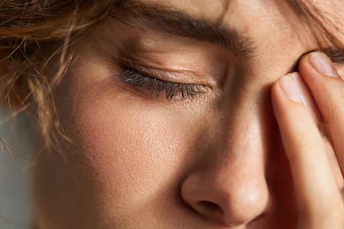 A close-up of a woman experiencing fatigue and rubbing her eyes, illustrating one potential early MS symptom.