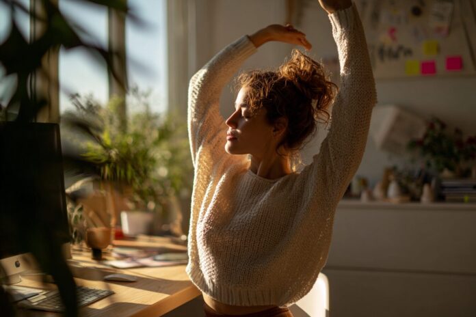 Woman stretching at her desk in a bright home office, representing Zone Zero movement.