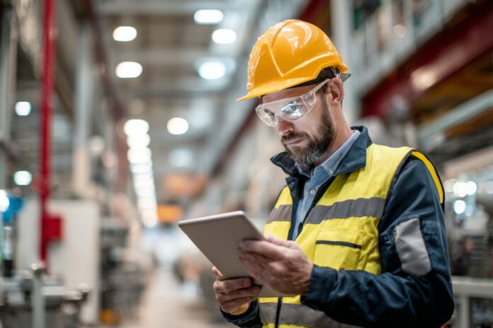 Industrial technician using tablet for real-time predictive maintenance in a factory environment.