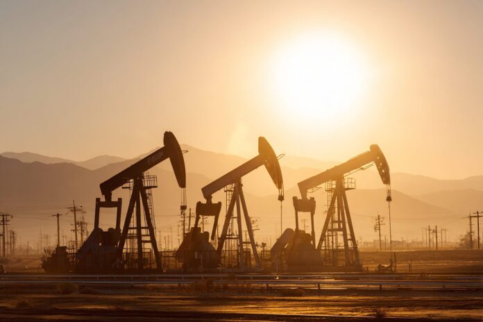 Row of inactive oil drilling rigs at a sunlit oil field showing little activity.