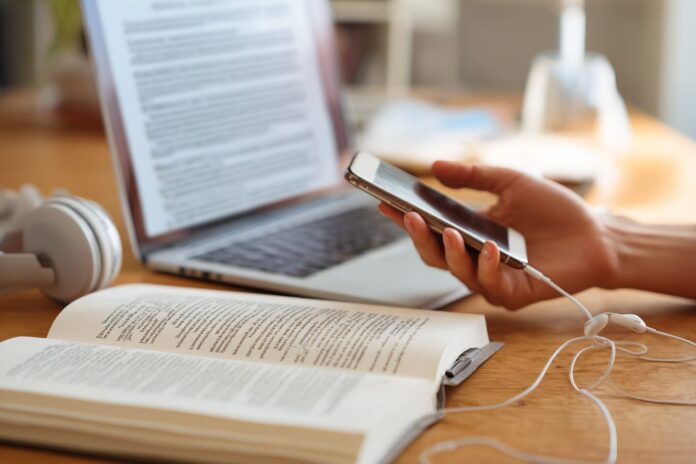 Person listening to a podcast on their smartphone while viewing a digital document on a laptop.