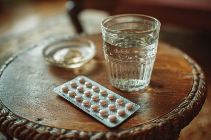 Blister pack of male birth control pills next to a glass of water on a table.