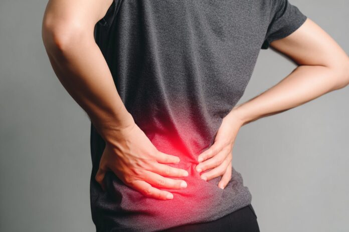 A person with visible spinal curvature holding their lower back in discomfort.