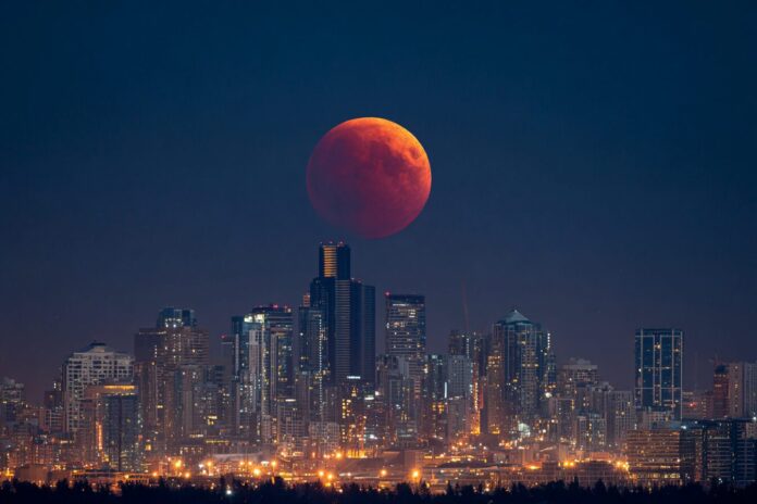 A dramatic red blood moon during the September 2025 total lunar eclipse, rising above an urban skyline.