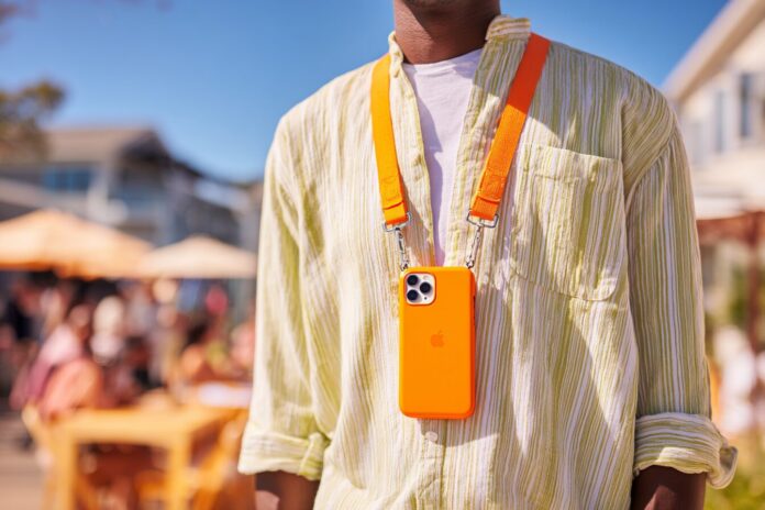 Apple Crossbody Strap attached to an iPhone draped across a model’s torso in a bright outdoor setting.