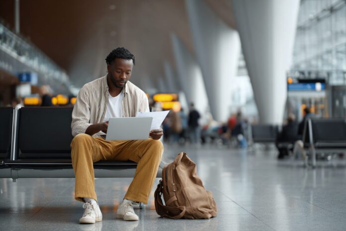 A tech employee reviewing travel documents at an airport with a laptop bag