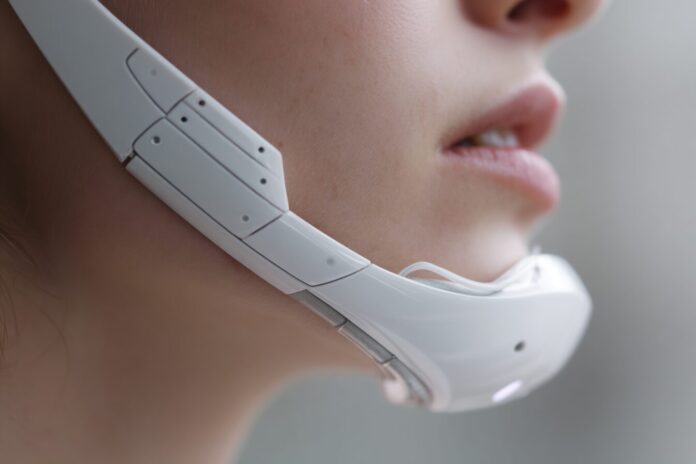 A futuristic white wearable device with sensors rests along a person's jaw line, hinting at subtle interaction with digital devices.