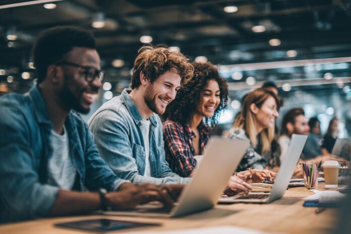 Group of diverse professionals using laptops and digital tablets in a modern workspace, symbolizing the impact of AI skills on career growth and salaries.