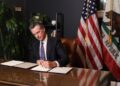 Gavin Newsom signing executive order at California capitol podium with prediction market screens in background